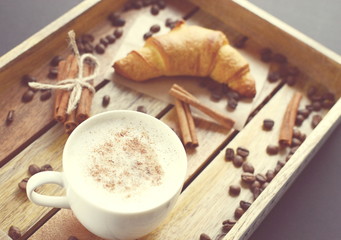 White cup of cappuccino and croissant on the wooden tray. Vintage style