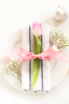 Elegance table setting with pink ribbon and tulip on white background. Spring romantic dinner. Top view.