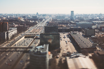 True tilt shift shooting of highway in metropolis from high point: multiple residential and office buildings, road intersection in focus with many cars on busy streets of the city, crosstown traffic