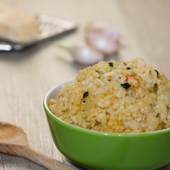 Serving of risotto (paella,pilaf)in green bowl, cheese grater, garlic and wooden ladle also present