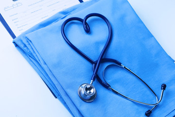 Medical stethoscope twisted in heart shape lying on patient medical history list and blue doctor uniform closeup. Medical help or insurance concept. Cardiology care, health, protection and prevention