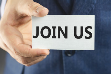 Business man in blue suit, close-up of hand showing card with text join us.