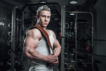 strong man in the gym is standing in side of with a belt on his shoulder