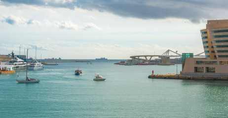 Boats navigating amongst moored counterparts in the harbor at Marina, Port Vell in Barcelona, Spain.  Ships out on the horizon, readying to offload their wares.