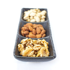 Assorted mixed nuts in black plate on white background