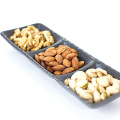 Assorted mixed nuts in black plate on white background