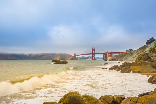 Spectacular bottom view of Golden Gate Bridge from Baker Beach, considered by many the most beautiful beach of San Francisco, California. Fog in summertime. Holidays, travel and leisure concept.