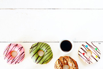 Cup of espresso and variety of donuts with different flavors (pistachio, vanilla, caramel, strawberry) on a white wooden table. Copy space.