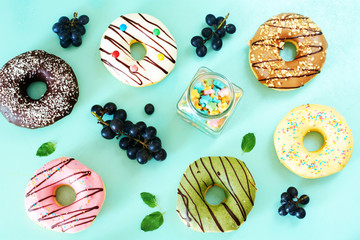 Assorted american donuts (vanilla, chocolate, strawberry, caramel, pictachio), grape and candy over light blue background. Top view. 