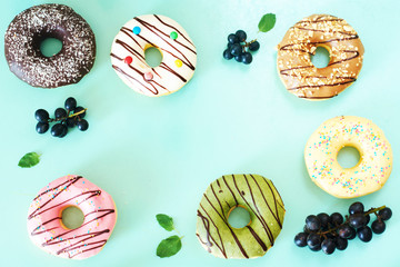 Assorted donuts frame over light blue background. Pistachio, caramel, strawberry, chocolate, vanilla donuts and grape. 