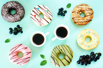 Coffee break with sweets. Assorted american donuts (vanilla, chocolate, strawberry, caramel, pictachio), two cups of black coffee, grape and candy over light blue background. 