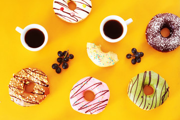 Two cups of espresso and variety of american donuts with different flavors (vanilla, chocolate, pistachio, caramel, strawberry) over warm yellow background. Coffee break with sweets. 
