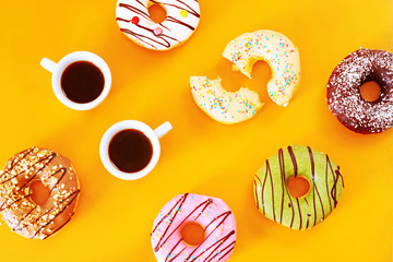 Two cups of espresso and assortment of american donuts (vanilla, chocolate, pistachio, caramel, strawberry) over warm yellow background. Coffee break with sweets. 