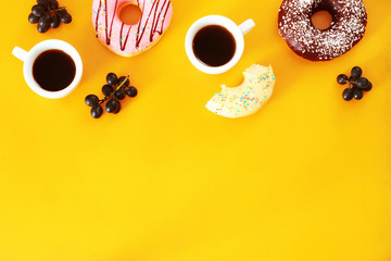 Sweet breakfast. Two cups of black coffee and assorted donuts: vanilla, strawberry, chocolate. Yellow background, copy space. 