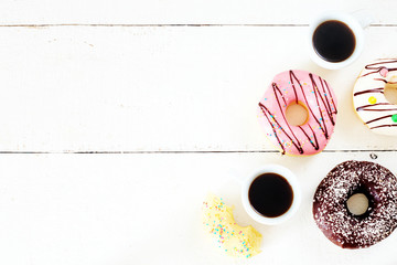 Assorted donuts with different flavors (chocolate, vanilla, strawberry) and two cups of black coffee over white table. Copy space.