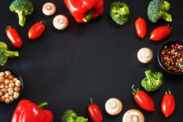 Vegetarian food frame over black background. Fresh cherry tomato, bell pepper, broccoli and champignons, ground pepper and cardamom. Copy space.