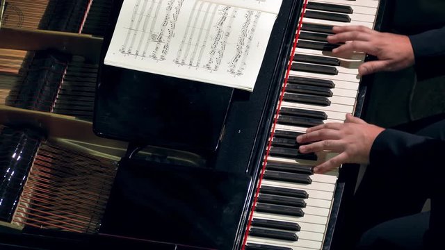Pianist plays open piano at a classical music concert. Music sheets of VII century classics (now public-domain). Hands and keyboard close-up.