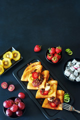 Crepes with strawberries, grapes, golden kiwi over dark board with a copy space. Copy space.