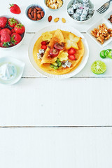 Vertical top view of healthy breakfast with crepes and exotic fruits. Thin pancakes with starfruit, dragon fruit, kiwi, banana, strawberries, walnut, almond and lime on a white table. Copy space.