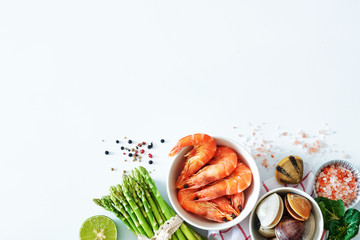 Top view of clean eating ingredients over white background with a copy space. Cooked prawns, clamps, asparagus, lime, salt and pepper.
