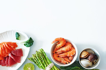 Salmon and tuna sashimi, shrimps, clamps and asparagus on a white table. Top view of light dinner ingredients with a copy space.