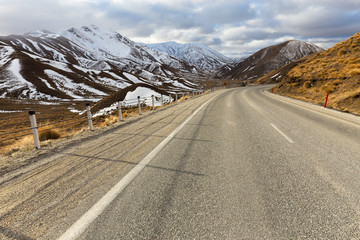 A winding alpine road disappears into the distance amongst snow capped mountains in New Zealand.