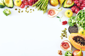 Clean-eating food frame with copy space. Top view of papaya, avocado, tomato, grape, asparagus, figs, broccoli, goji, chia, pumpkin seeds on white background.