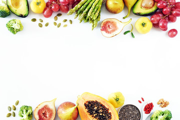 Fresh fruits and vegetables food frame over white background with empty space. Top view of papaya, avocado, tomato, grape, asparagus, figs, broccoli, goji, chia, pumpkin seeds. 