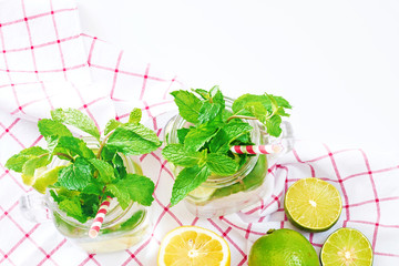 Close-up of two mason jars with mojito or mint and lime lemonade, fresh citrus fruit on a white table with copy space. Selective focus.