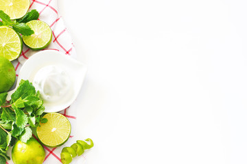 Top view of fresh lime, mint and juicer on a white table with copy space. Making lemonade or mojito background.