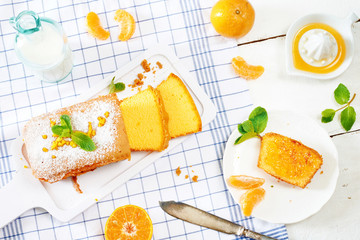 Top view of sweet breakfast with orange sponge cake, mandarin, fresh milk and jam on white and blue vichy towel. 