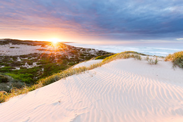 The sun bursts above the horizon, illuminated the sand dunes and surrounding coastline in this beautiful seascape.