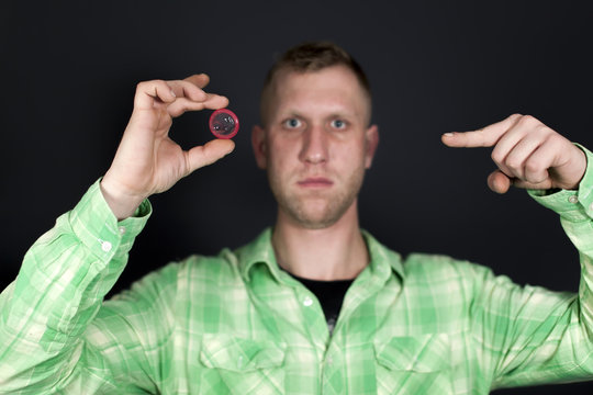 
Man show for finger on  red condom in front of dark background. Sign OK 
