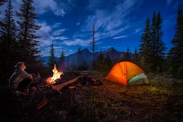 Foto auf Acrylglas Camping Mann, der nachts neben Lagerfeuer und Zelt zu den Sternen aufschaut