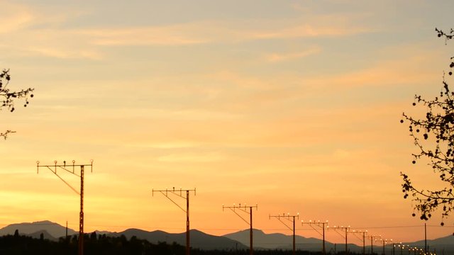 Airplane landing at airport at sunset with lighted lamp posts