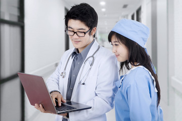 Asian doctors use laptop in corridor