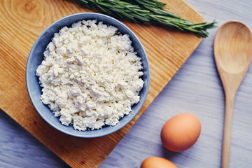 Curd in a cup, eggs and wooden spoon lying on a table.