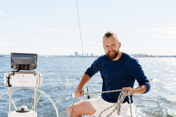 Handsome, bearded guy winding a rope on a yacht. Traveling, vacation, holiday, concept.