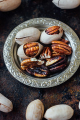 Pecan nuts on metal plate over black rustic surface.