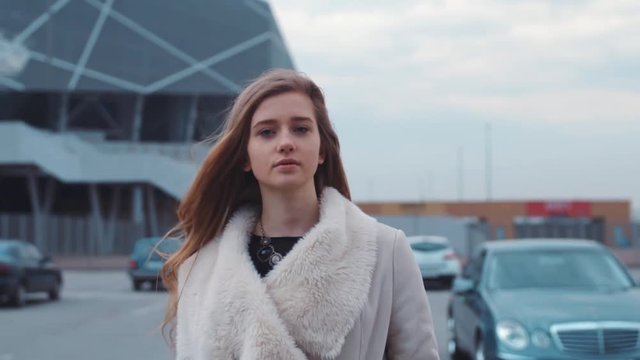 Portrait of a nice beautiful self-confident young woman going through parking with her hair loose and light wind blowing in her face.