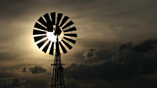 A windmill turning in the wind against a setting sun and storm clouds