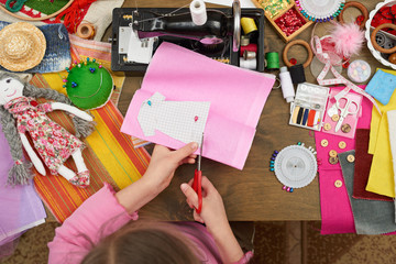 Fototapeta premium girl sews doll clothes, top view, sewing accessories top view, seamstress workplace, many object for needlework, handmade and handicraft