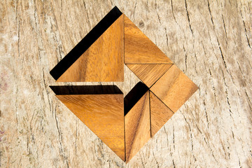 Tangram puzzle as arrow in square shape on wooden background (Concept for business direction and decision)