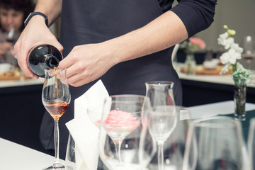 Sommelier pouring rose wine to the wine glass. Serving table prepared for event party or wedding. Soft focus, selective focus. Toned.