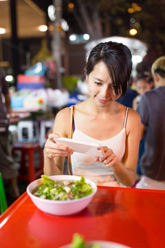 Woman taking photo on her food in outdoor market in Bangkok city