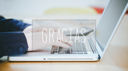 Gracias, Spanish text for Thanks text over young man typing on laptop at desk