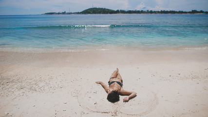 Fototapeta na wymiar The beach on the island of Bali. Girl in a black bathing suit lying on a sandy beach and resting. Its soothing sand, sunny, clean and turquoise ocean island.