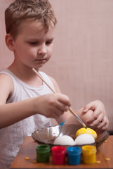 A little boy paints the eggs on the eve of Easter, colorful paints and brush,