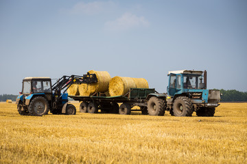Vinnitsa,Ukraine - July 26,2016.huge tractor collecting haystack in the field at nice blue sunny day,Tractor collecting straw bales,Agricultural machine collecting bales of hay,harvest concept