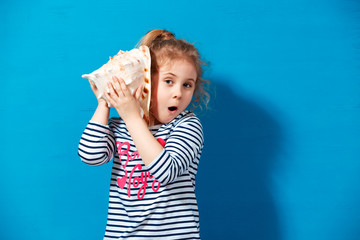 Portrait of blonde child girl listen a seashell at the blue wall. Summer vacation concept